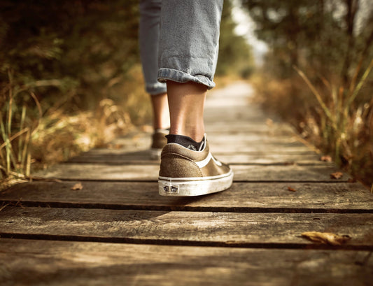a wooden pathway, image includes a womans lower legs wearing trainers walking along the pathway